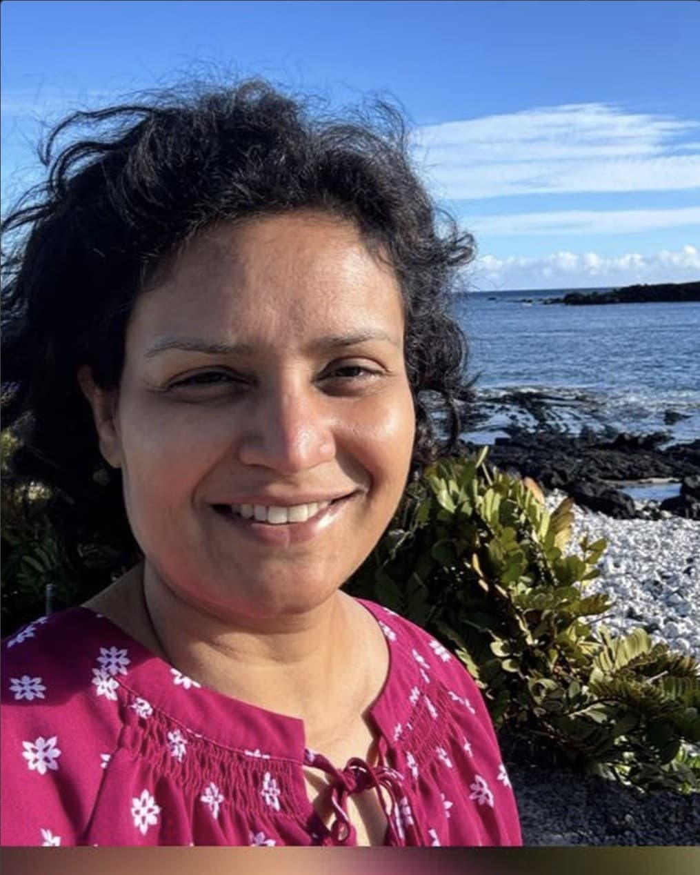Saroja, QHHT certified Chakra Healing Hypnosis practitioner, smiling on a coastal shoreline